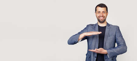 Young businessman man with a beard in a jacket, gesturing with his hands showing a large and large...
