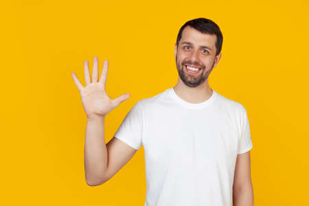 Modern young man with a beard in a white tank top shows number five with fingers on hand, smiling confidently and happily, looking at the camera. The man shows five fingers. Number 5 yellow backgroundの写真素材