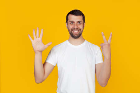 Modern young man with a beard in a white tank top shows number seven with fingers on hand, smiling confidently and happily, looking into the camera. The man shows seven fingers. Number 7.の写真素材