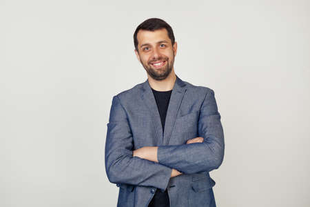 Young businessman with a smile man with a beard in a jacket, happy face, smiling with crossed arms, looking at the camera. A positive person. Portrait of a man on a gray background.の写真素材
