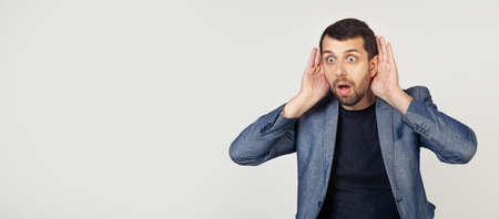 Young businessman man with a beard tries to hear both hands on his ear, curious about gossip....