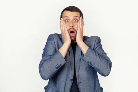 Young businessman man with a beard scared and shocked, surprised and surprised with hands on his...
