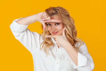 Blond woman in white shirt, middle aged european girl, designer creating a new project, looking at the footage and smiling, rendering, creating the perfect shot, standing against yellow backgroundの写真素材