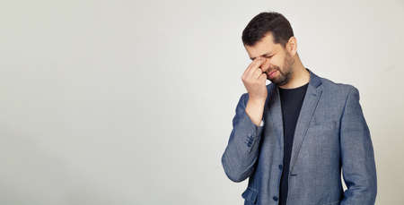 Young businessman man with a beard in a jacket, tired of rubbing his nose and eyes, feeling tired...