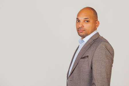 Handsome young male African American businessman in jacket looking at the camera holding his head in three quarters with a serious expression on his face. posing for a photo on a gray background.の写真素材