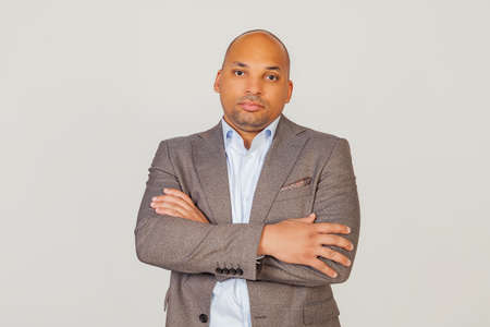 Handsome young male African American businessman in a jacket crossing his arms over his chest, looking at the camera with a flirty facial expression. posing for a photo on a gray backgroundの写真素材