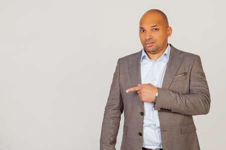 Male African American businessman in a jacket pointing with hand and finger with an expression of disgust. Copy space. on a gray backgroundの写真素材