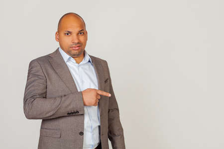 Male African American businessman in a jacket pointing with hand and finger with an expression of disgust. Copy space. on a gray backgroundの写真素材