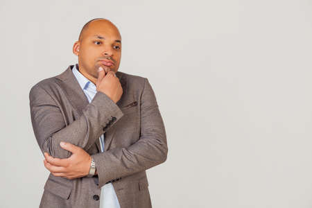 Handsome young male African American, businessman in jacket looking to the side and thinking touching chin with hand looking to the side with pensive facial expression.の写真素材