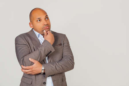 Handsome young male African American, businessman in jacket looking to the side and thinking touching chin with hand looking to the side with pensive facial expression.の写真素材