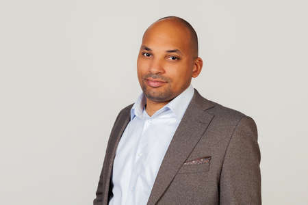 Male African American businessman in jacket posing in three quarters, looking at the camera and smiling happily. Lifestyle concept. on a gray backgroundの写真素材