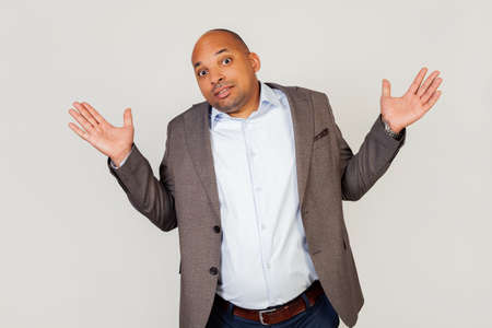 Young male African American businessman, shrugs, clueless and confused expression with raised arms and hands. Doubt conceptの写真素材