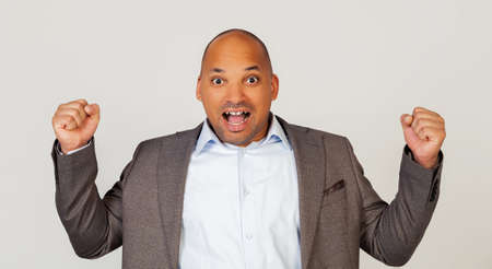 Excited young man african american businessman shouting loudly and expressively gesturing with his hands, joyful positive man clenching his fists, celebrating his success. Successの写真素材