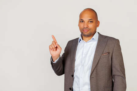 Young male African American businessman pointing his finger upwards with a smiling face. Pointing hand and finger to the side, looking into the camera. Copy space for your adの写真素材