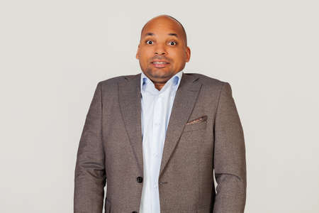 Annoyed African American guy businessman frowns with displeasure, annoyed with bad news, feeling disgusted and displeased, looks excited, gesturing funny and comical. Standing on a gray backgroundの写真素材
