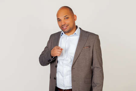 Portrait of young african american guy businessman pointing with index finger at camera and smiling brightly. Standing on a gray backgroundの写真素材