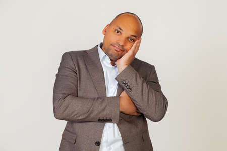 Portrait of a young african american guy businessman holding his hand on his face and staring indifferently at the camera, thinks he looks tired and depressed with crossed arms. gray background.の写真素材