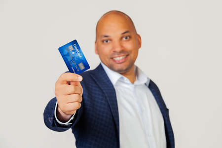 Portrait of a happy young African American businessman guy holding a credit card with a happy face, stands and smiles with a confident smile showing teeth. Standing on a gray backgroundの写真素材