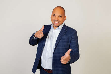 Portrait of a successful young African American businessman guy pointing his fingers at the camera with a happy and funny face. Good energy and vibes. Standing on a gray backgroundの写真素材