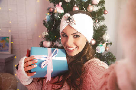 Self-portrait of a cheerful rejoicing girl removing a gift box with a Christmas tree behind her...