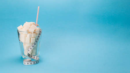 Glass cup with a straw full of cubes of white sugar on a blue background. A measuring tape is wrapped around the glass. Diabetes conceptsの写真素材