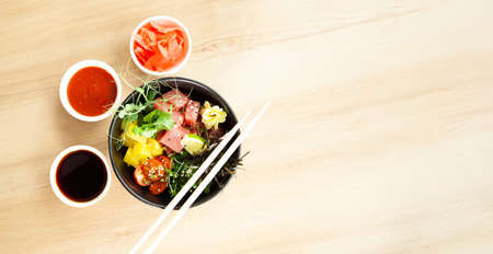 Poke salad with tuna in a bowl. Ingredients fresh tuna, cherry tomatoes, marinated seaweed, rice, takuan, Ponzu sauce, Teriyaki sauce, nori, sesame seeds, lime, cilantro. Asian seafood salad concept.の写真素材