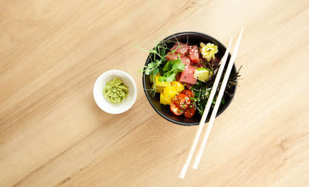 Poke salad with tuna in a bowl. Ingredients fresh tuna, cherry tomatoes, marinated seaweed, rice, takuan, Ponzu sauce, Teriyaki sauce, nori, sesame seeds, lime, cilantro. Asian seafood salad concept.の写真素材