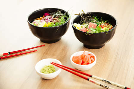 Two poke salads with beef and tuna in a bowl on a restaurant table. Poke salads in a bowl next to chopsticks and ginger with wasabi. Asian salad concept.の写真素材