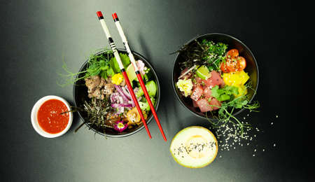 Poke salads with tuna and beef in bowls on the table. Two bowls of poke salad with chopsticks on a gray background. Asian seafood salad conceptの写真素材