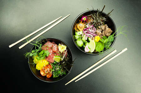 Poke salads with tuna and beef in bowls on the table. Two bowls of poke salad with chopsticks on a gray background. Asian seafood salad conceptの写真素材