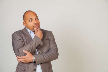 Serious pensive African man male, touching his chin, looking to the side, thinking about a solution in search of creative ideas concept. Solves business problems or adopts a solution conceptの写真素材