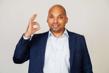Young african american man smiling positively, making okay hand and fingers sign. Lucky expression. Black man feeling successful and contented, smiling making a sign ok with his handの写真素材