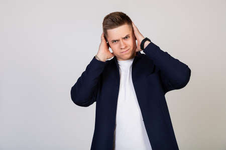 A young man covering his ears with his hands, he does not want to listen to news, gossip, information. Bearing terrible pain. Young guy covered his ears with his hands so as not to hear rumorsの写真素材