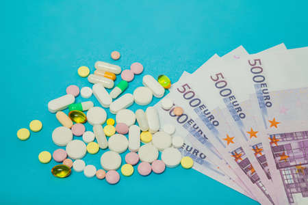 Medicine pills over euro banknotes on a blue background. Covid-19 coronavirus pills are on the euro...