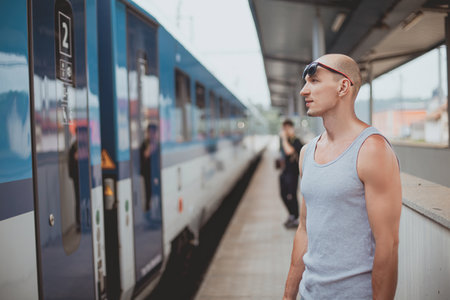 Young man in a t-shirt on the platform waiting for a train using mobile phone. Man by train station...