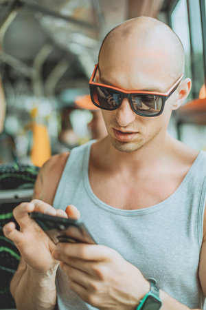 Young mansmartphone travelling by bus in city. A young man wearing a T-shirt and sunglasses uses a...