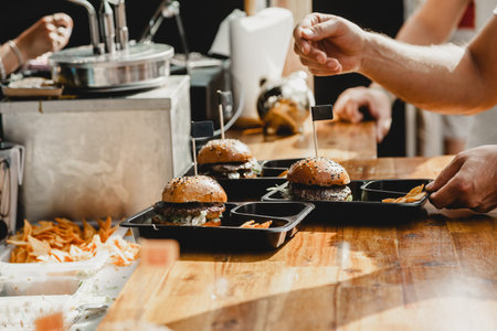 Man holds in his hand burgers at a burger feast. Dinner Hamburger Food Feast Party. Big burger in hands at street food outdoor festival. Festival food dayの写真素材