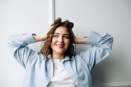 Image of attractive happy cheerful female student with curly hair and sincere smile enjoying weekend morning at home, dancing in kitchen, feeling carefree and relaxed, looking awayの写真素材