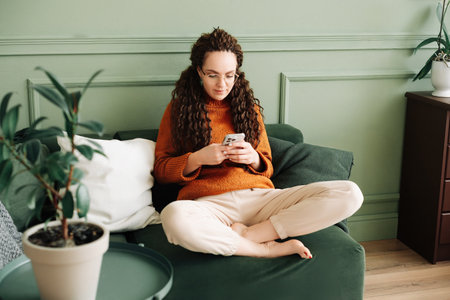Happy Woman Relaxing on Sofa Using Cell Phone for Shopping and Social Media at Home - Ecommerce and Social Media Conceptの写真素材