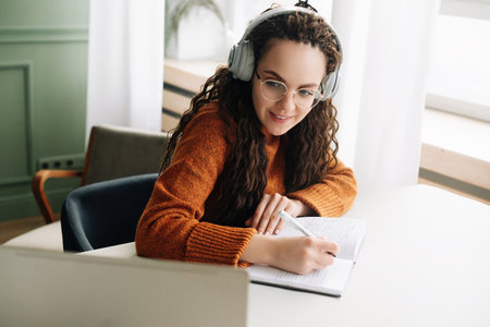 Happy young woman elearning on laptop from home attending webinar with headphones. Smiling student watching virtual class or having web conference meeting on computer.の写真素材