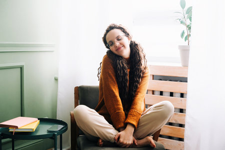 Young woman feeling joyful and relaxed at home. Happy woman enjoying a cozy day at home. Smiling lady feeling content and relaxed in her modern apartment.の写真素材