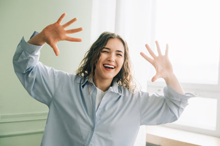 Joyful housewife having fun dancing in the living room, enjoying her free time at home while kids are at school. Happy housewife woman making faces.の写真素材