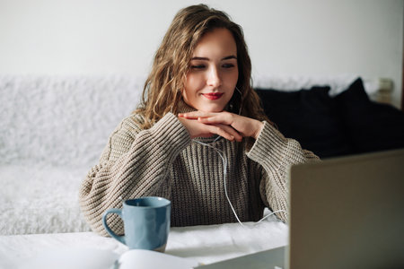 Engaged female freelancer in video conference with employer, attentively discussing project details, smiling at web camera with folded hands under chin.の写真素材