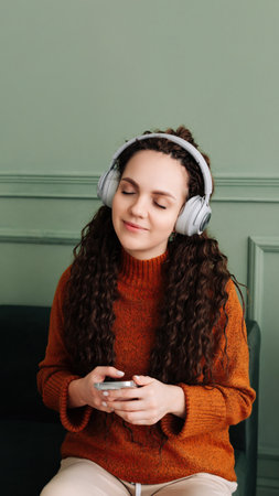 A calm, relaxed, carefree young woman listens to music, an audio podcast or audiobook on her cell phone while sitting at home, meditating and relaxing, feeling peace of mind with her eyes closed.の写真素材