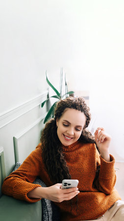 Happy lady browsing e-commerce sites or watching funny videos on a smartphone Enjoying online leisure. A smiling young woman uses a cell phone for online shopping or entertainment at home on the couchの写真素材