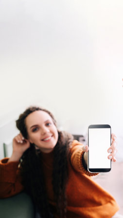 Happy young woman holding mobile phone to showcase blank display for app advertising. Smartphone mockup screen for advertising digital application with womans hand.の写真素材