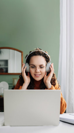 Young happy woman student wearing headphone using laptop elearning at home office listening music, live lecture or podcast webinar, learning language on online seminar sitting at desk with computer.の写真素材