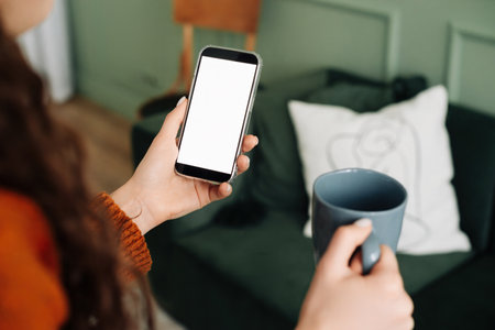Mockup Smartphone Display: Woman Holding Coffee and Texting on Cellphone Apps, Over Shoulder View for Advertising and Promotions. smartphone with a blank screen for mobile application layoutの写真素材