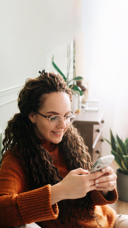 Happy young woman using smartphone for online shopping on couch at home. Relaxed lady enjoying technology and mobile apps for e-commerce.の写真素材