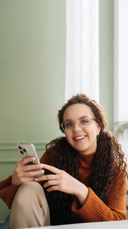 Happy woman using cell phone technology at home, smiling while checking apps on her smartphone and relaxing with cellular devices in hand.の写真素材